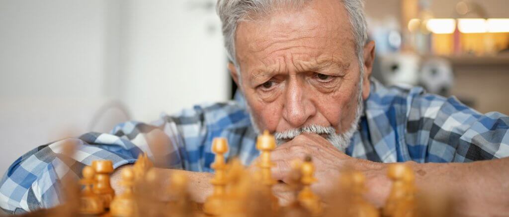 A senior man is thinking about his next chess move.